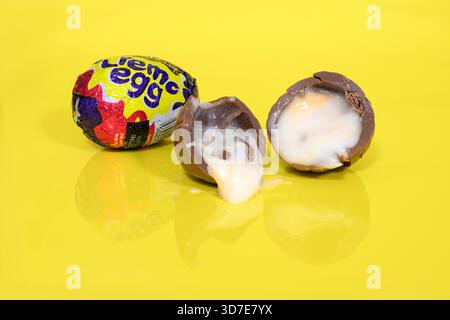 Cadbury Creme eggs on yellow background with one cut in half showing the gooey fondant oozing out Stock Photo