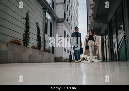 Couple walking together on urban sidewalk, professional attire, stylish vibe, city architecture backdrop during afternoon Stock Photo