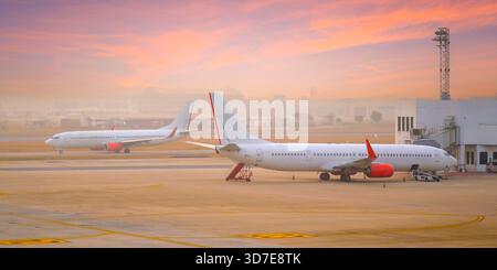 Commercial passenger airplane during taxi movement for take off, and another boarding passenger for flight early morning. Stock Photo