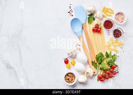 Food background with place for text, with different kinds of pasta, tomatoes, herbs, mushrooms, eggs, seasonings scattered on light marble background, top view. Italian cuisine concept Stock Photo