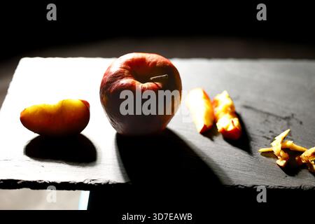 Red apple with a large bright slice placed on a slate board, illuminated by warm studio light. Ideal for food styling, healthy lifestyle, and minimali Stock Photo