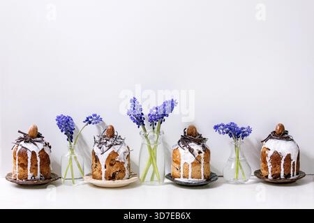 Homemade traditionla small Easter kulich cakes with chocolate nests and eggs on plates in row decorated with muscari flowers over white marble table. Traditional ortodox Easter Russian Ukrainian bake Stock Photo