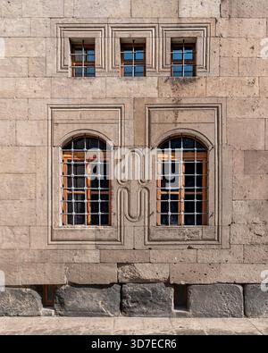 Stone facade with barred rectangular and arched windows, featuring carved frames and stylized geometric patterns. Stock Photo