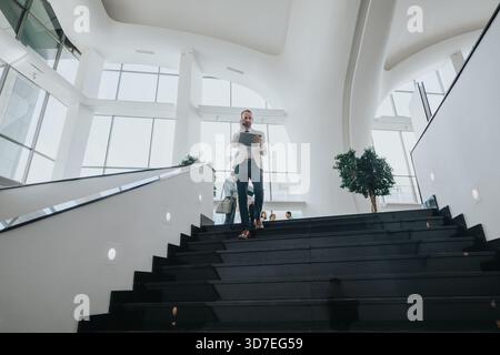 Businessman on stylish black staircase in a bright modern office using tablet and phone today Stock Photo