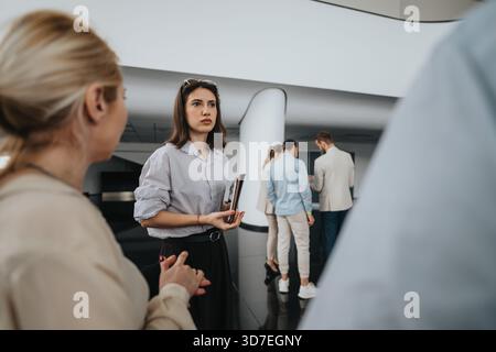 Business colleagues gather in a modern lobby, preparing for a meeting and discussing documents in a sleek office setting Stock Photo