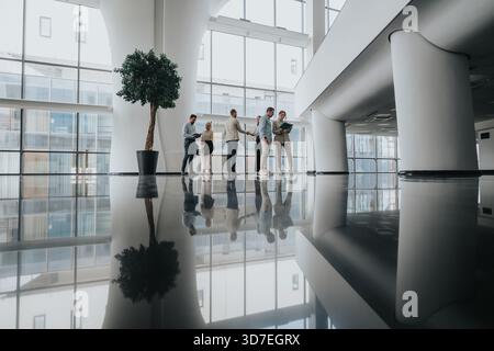 Group of colleagues in a modern office lobby discussing and shaking hands during a break Stock Photo