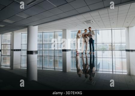 Three colleagues review a tablet in a modern office lobby, preparing for a business meeting Stock Photo