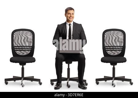 Businessman with a laptop computer sitting in an office chair between two empty chairs isolated on white background Stock Photo