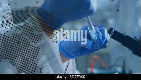 Using pipette, researcher in PPE transferring into vial at bench, microscope arm and map overlay Stock Photo
