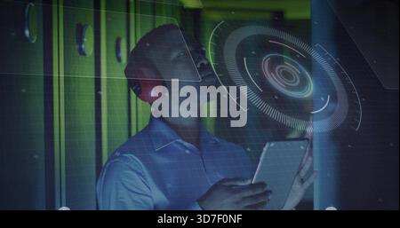 Holding tablet, tech wearing light-blue shirt and red earmuffs inspecting holo UI in tech corridor Stock Photo