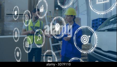 Discussing two warehouse workers wearing helmet hi-vis vest using tablet with floating AR icons Stock Photo