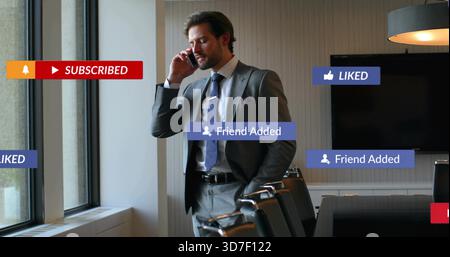 Talking mid-adult man in grey suit holding smartphone in meeting room, showing social overlays Stock Photo
