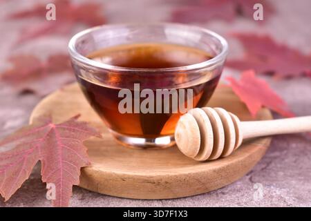Maple syrup in a small glass bowl on a wooden tray. Close-up. Stock Photo