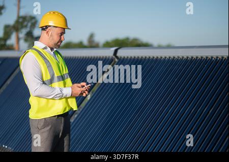 Unrecognizable technician checking data on phone while standing by solar installation Stock Photo
