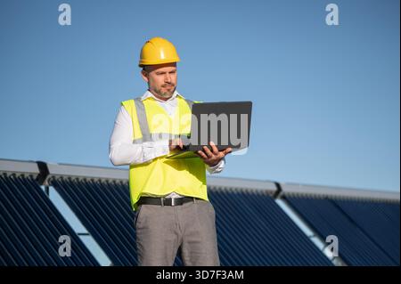 Worker with hard hat working on digital computer among solar panels Stock Photo
