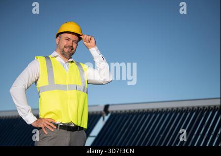 Technician in safety vest standing near solar panel field on rooftop Stock Photo