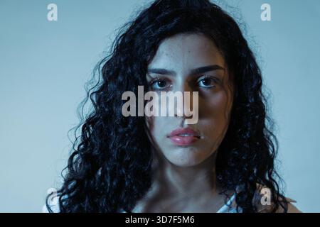Young woman with curly hair and serious expression looking at camera Stock Photo