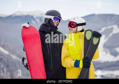 Smiling teenage friends, snowboarder and skier, standing together on snowy mountain slope during winter vacation, active lifestyle concept. Stock Photo