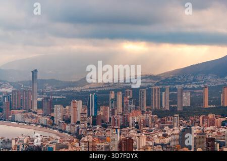 A detailed, wide-angle shot of the Benidorm skyline where the sunlight dramatically breaks through the clouds, Stock Photo