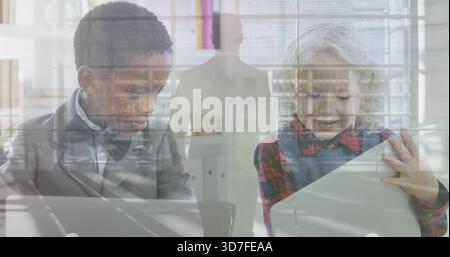 Sitting two kids using laptop, tablet at desks, in jacket, pinafore, adult suit, window reflections Stock Photo
