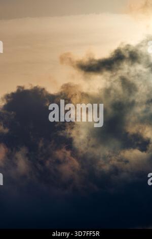A vertical composition focusing on a towering mass of dark, brooding clouds, dramatically illuminated by a bright, warm-toned sky above. Stock Photo
