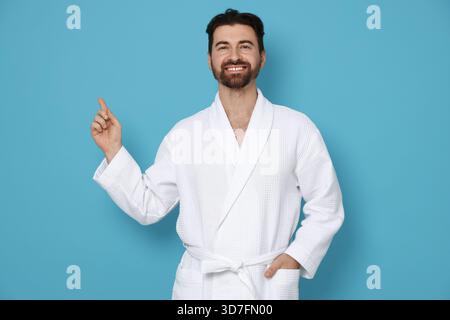 Man in bathrobe pointing at something on light blue background Stock Photo