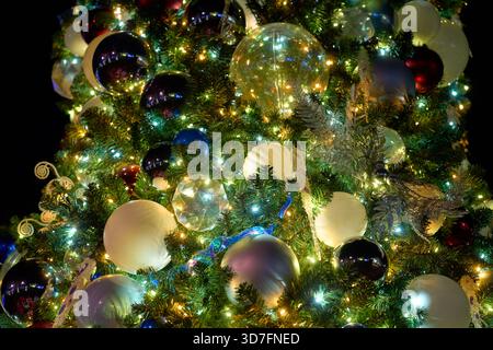 White, silver, and colorful baubles fill the evergreen branches. Tiny LEDs and tinsel create a sparkling holiday glow. Stock Photo