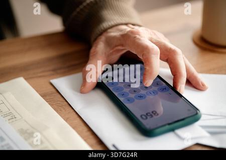 Senior Woman Calculating Expenses Using Smartphone While Analyzing Bills Stock Photo