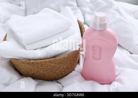 Laundry basket with folded towels and bottle of detergent on bed linens, closeup Stock Photo