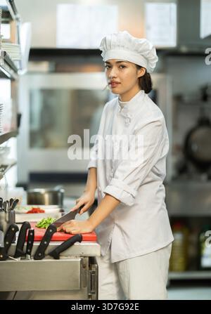 Young female chef chops ingredients for dish Stock Photo