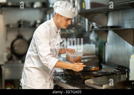 Young male chef prepares dish in frying pan Stock Photo