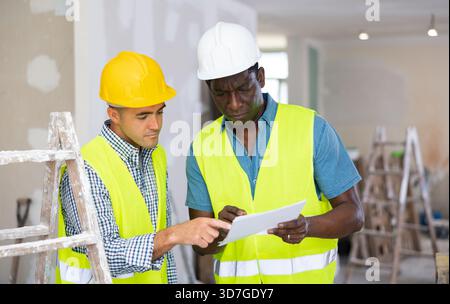 Two engineers discussing blueprints in renovated room Stock Photo