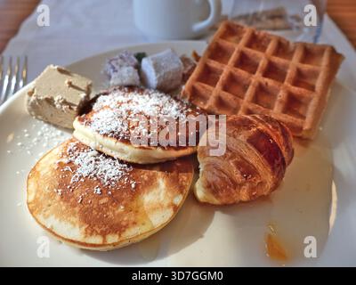 A generous breakfast plate featuring fluffy pancakes dusted with powdered sugar, a glazed waffle, buttery croissant, and assorted pastries arranged on Stock Photo