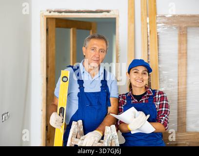 Happy woman and man, professional repairmen standing with waterpas and paper in the middle of the construction site Stock Photo