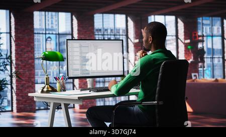 African American IT expert working with a computer full of code. Professional system engineer focuses on software development, debugging, encryption and system security at home. Camera A. Stock Photo