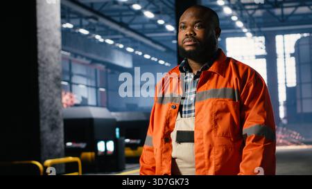 African american man overseeing equipment during assembly in warehouse, illustrating manufacturing development with industrial labor and manpower. Steel production workshop. Stock Photo