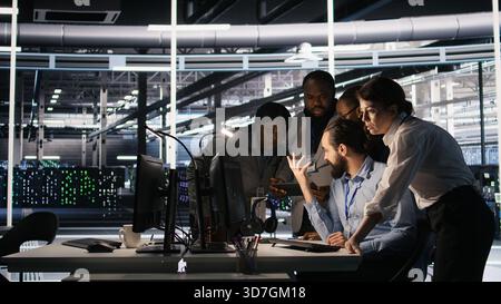 Data center system administrators performing maintenance on supercomputers used for AI processing. Team managing server hub rigs used for deep learning training, looking over business charts, camera A Stock Photo