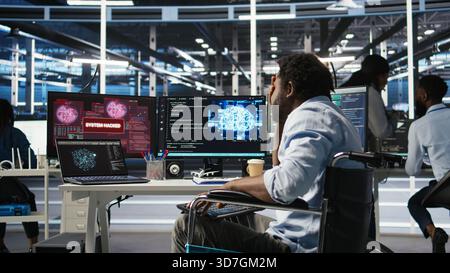 Man with paraplegia in server hub trying to protect hardware from hacker attack stealing sensitive information. Data center specialist in wheelchair fighting virus during security breach, camera A Stock Photo