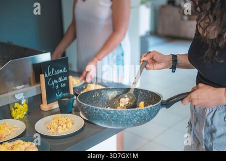 A home cook is in her kitchen preparing a delicious breakfast, holding a frying pan with fried eggs. Stock Photo