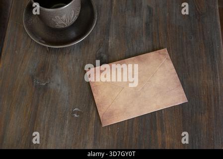 Textured brown envelope resting on a dark wooden surface with a coffee cup Stock Photo