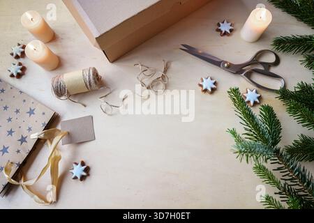 Wrapping supplies for Christmas gifts such as cardboard box, scissors, paper, tying cord, candles and pine branches, natural colors, copy space, top v Stock Photo