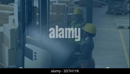 Operating forklift, man and woman wearing hard hats checking inventory with clipboard in warehouse Stock Photo