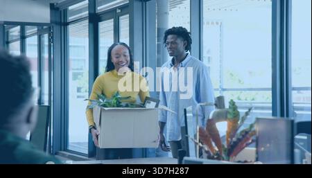 Carrying cardboard box with plant and frame, woman in mustard-yellow top walking into modern office Stock Photo