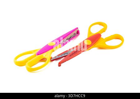 Two colorful decorative pattern-cutting craft scissors, one pink and one red, with yellow handles, isolated on white. Stock Photo