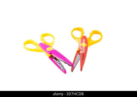 Two colorful decorative pattern-cutting craft scissors, one pink and one red, with yellow handles, isolated on white. Stock Photo