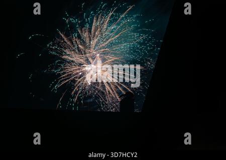 A complex and colorful firework burst combining warm golden and cool teal/green streaks, creating a spectacular display against the deep black night s Stock Photo
