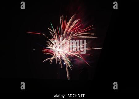 A powerful, single firework exploding into vibrant streaks of red, white, and green against the black night sky, captured from a low angle with a dark Stock Photo