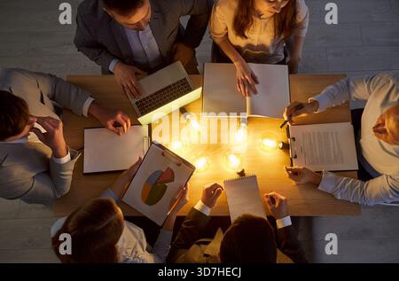 Business people discussing company finance sitting at desk with lightbulbs in office. Stock Photo
