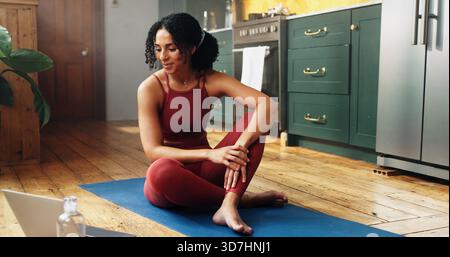 Happy woman, laptop and yoga with online tutorial in kitchen for health tips or exercise on mat. Female person, yogi or streaming with computer for Stock Photo