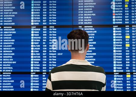 Traveler checks the flight information board at the airport terminal. Toronto, ON Stock Photo